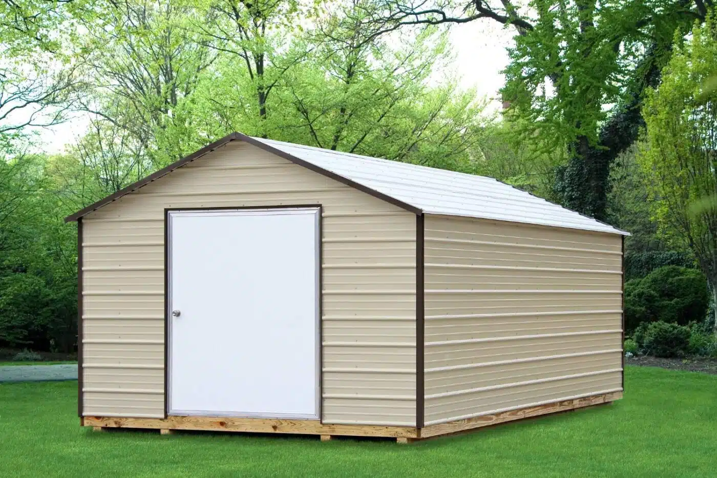 Shed on wooden foundation in grassy field. Beige, metal seam siding and roof