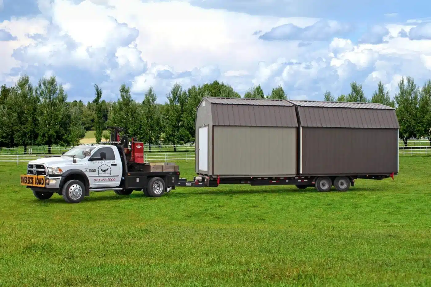 Bald Eagle Barn truck with two bald eagle barn sheds on back in grassy field with white fence in the background