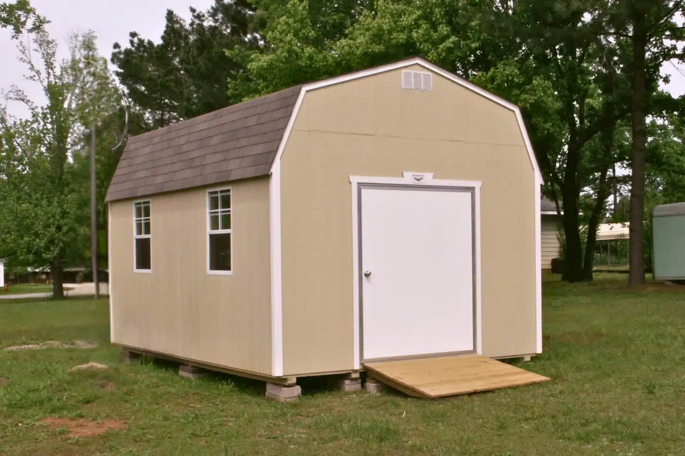 Bald Eagle Barn set on concrete block foundation installed by bald eagle barn builders. Beige barn style shed with white door and trim. Shingled roof and wooden ramp.